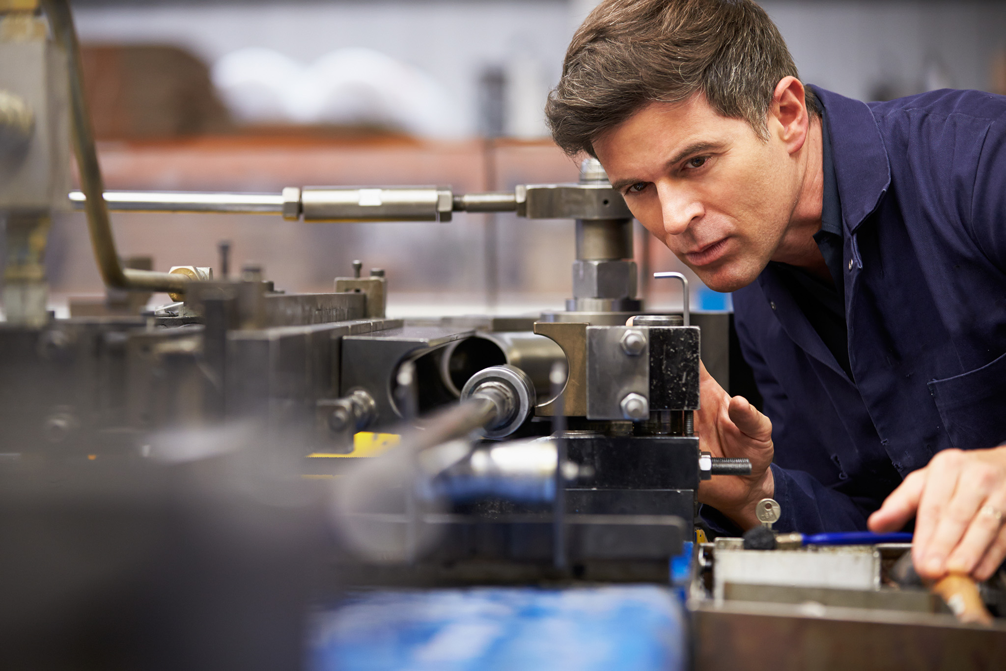 A male engineer in blue overalls inspects a piece of machinery